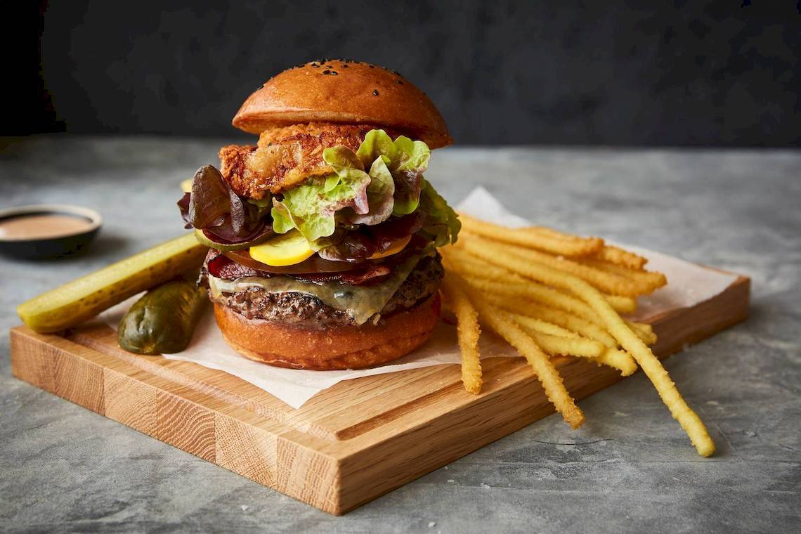 Ein Burger mit Pommes und Gurken auf einem Holzschneidbrett.