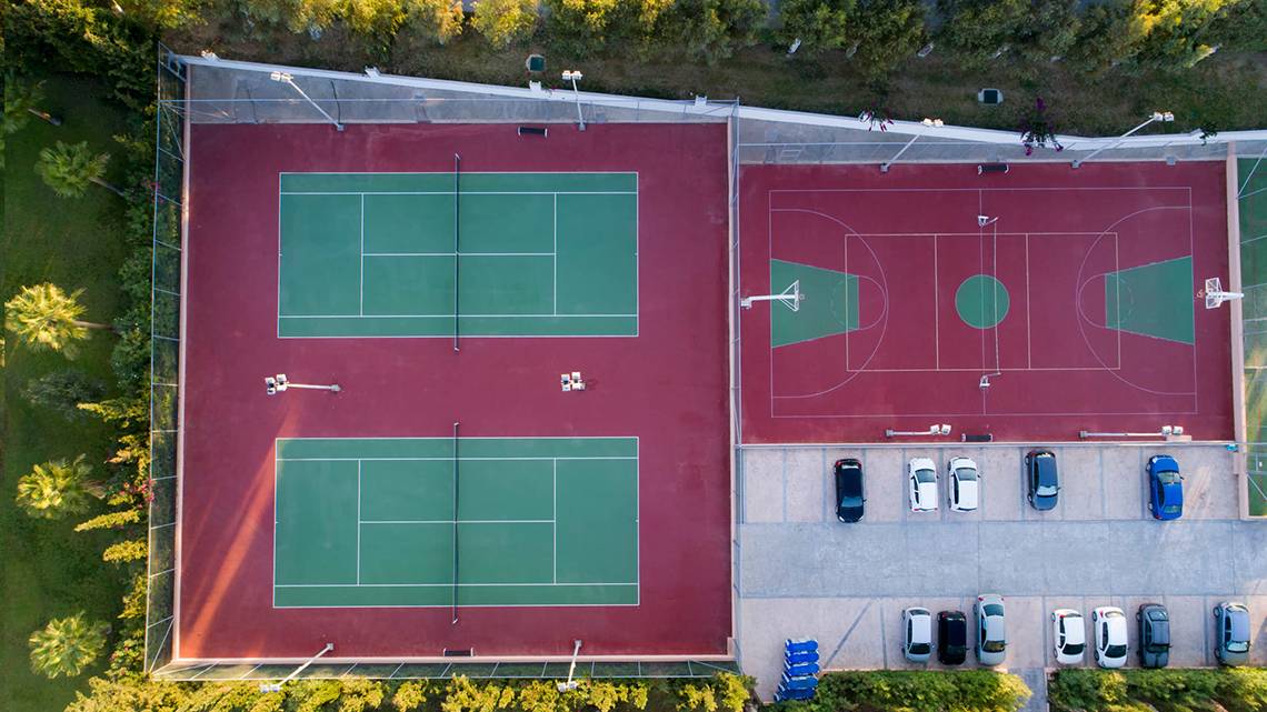 Luftaufnahme der Sportanlage des Horizon Beach Resorts mit Tennis- und Basketballplätzen und geparkten Autos.
