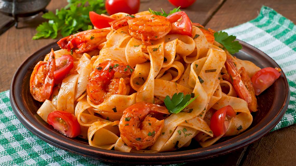 Ein Teller mit gebratenen Garnelen und Nudeln, garniert mit Tomaten und Petersilie.