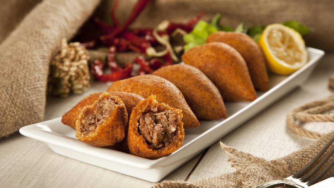 Orientalische Fleischspieße auf einem weißen Teller, begleitet von Salat und Paprika.