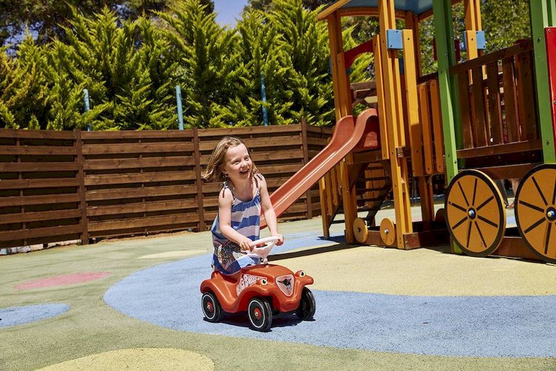 Ein kleines Mädchen spielt auf einem roten Spielzeugauto im Spielplatz des Robinson Kyllini Beach.