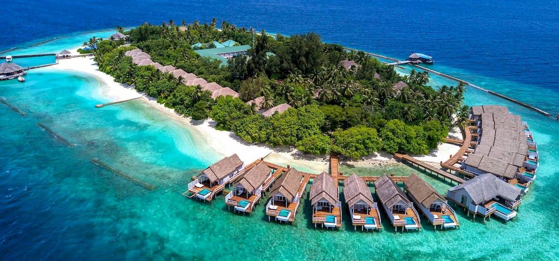 Luftaufnahme des Amaya Kuda Rah Hotels auf einer Insel mit mehreren Wasserbungalows und türkisfarbenem Wasser.
