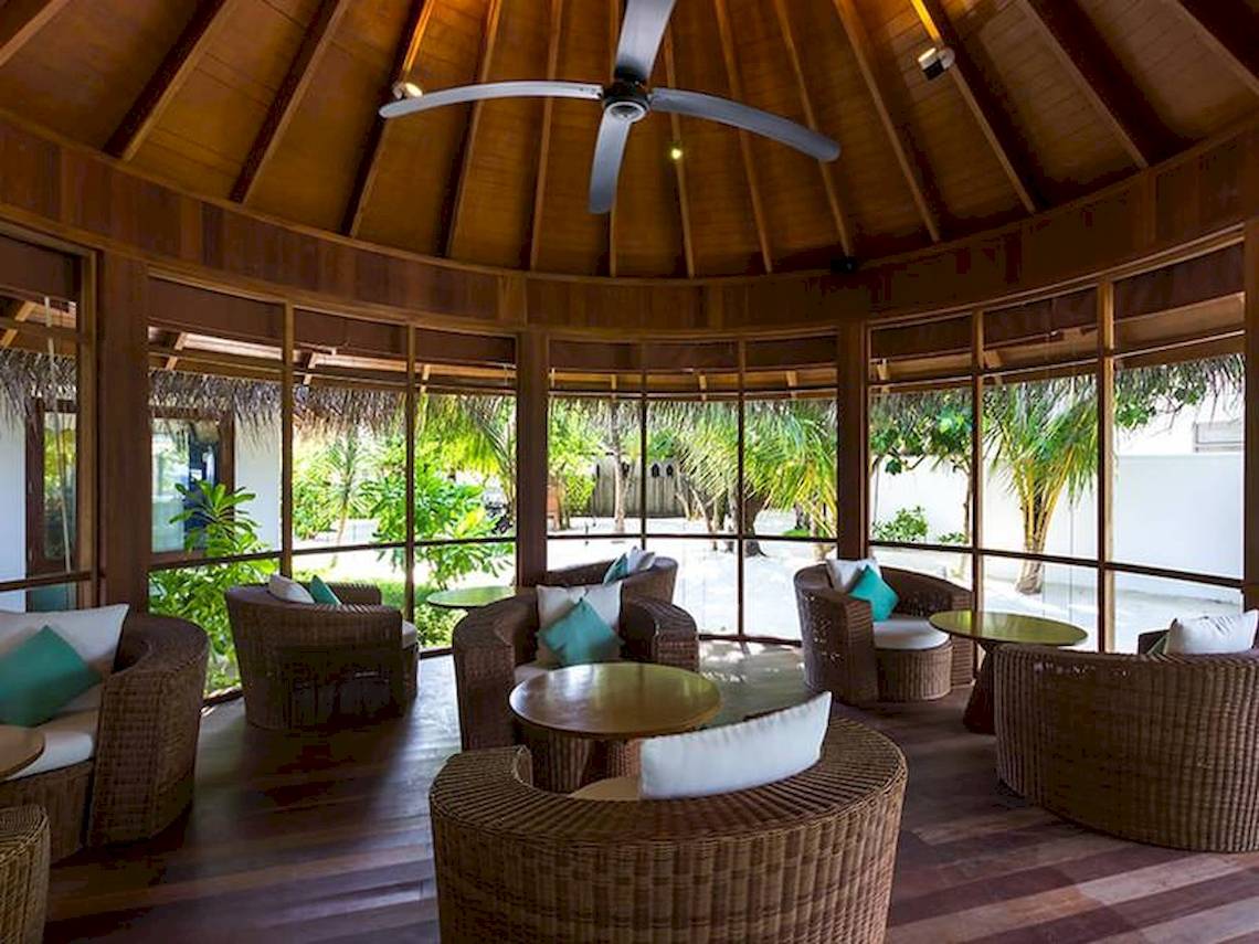 Loungebereich im Amaya Kuda Rah Hotel mit Korbsesseln, Tischen und Glaswänden.