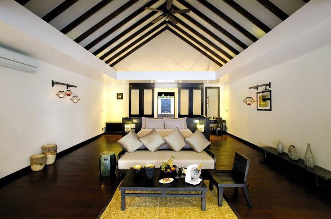 Schlafzimmer im Atmosphere Kanifushi Maldives Hotel mit Bett, Couch, Tisch und Dekor.