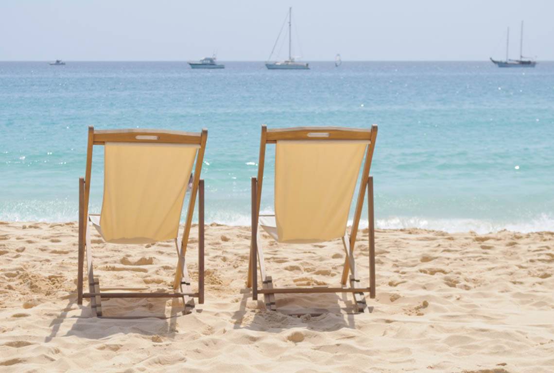 Zwei Liegestühle auf dem Strand mit Booten im Hintergrund im Oasis Salinas Sea Hotel.