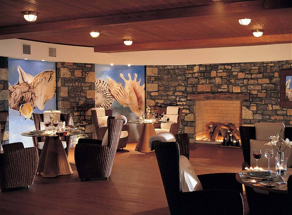 Innenbereich des Elounda Beach Hotel & Villas mit Steinwänden, Tischen und Stühlen.