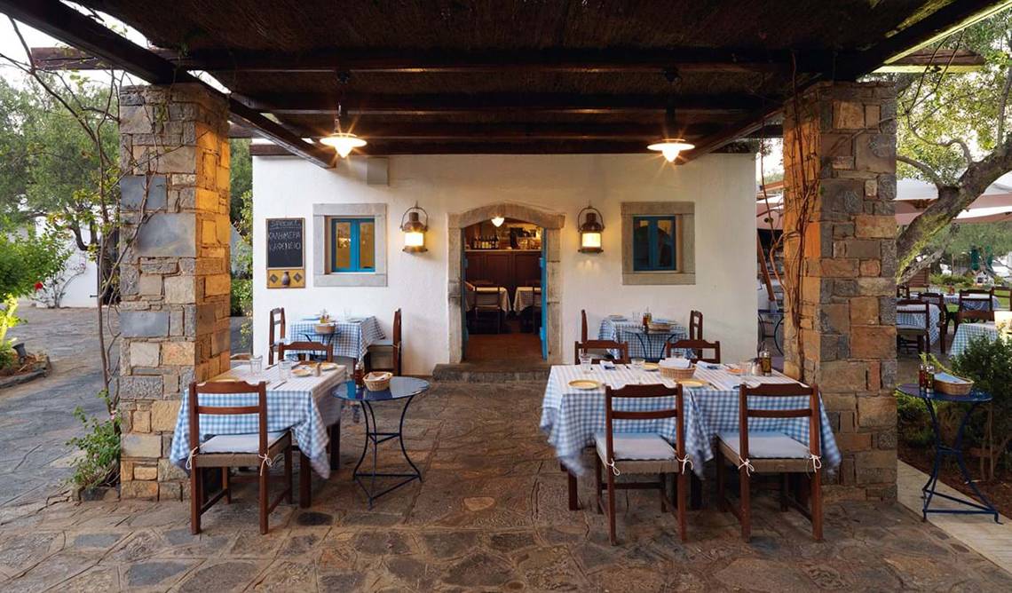 Außenbereich des Elounda Beach Hotel & Villas mit blau-weiß karierten Tischdecken und Steinsäulen.