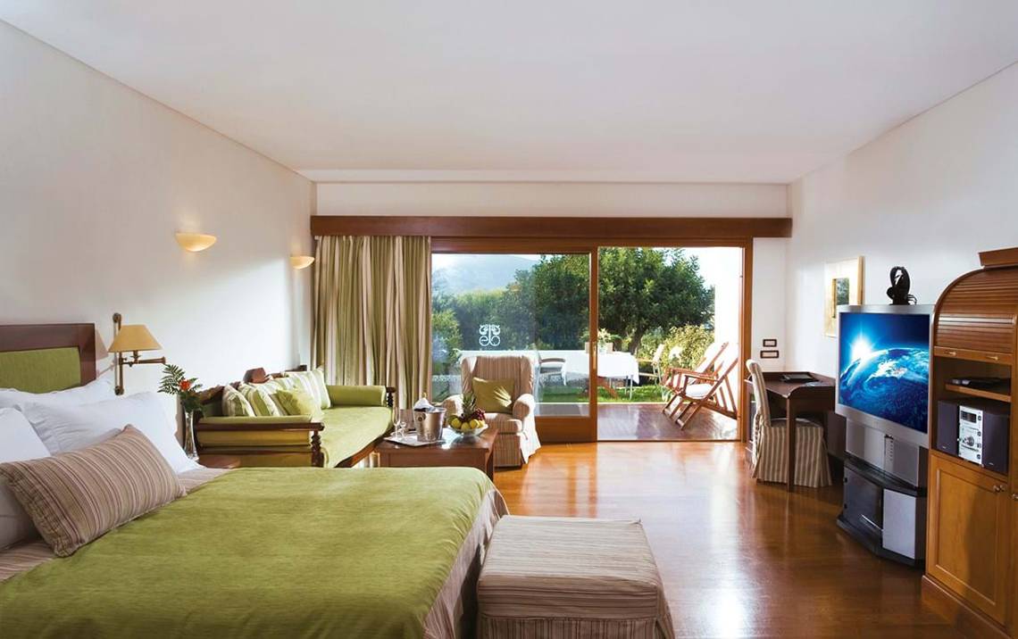 Innenansicht einer Suite im Elounda Beach Hotel & Villas mit großem Bett, Wohnzimmer und Terrassenzugang.