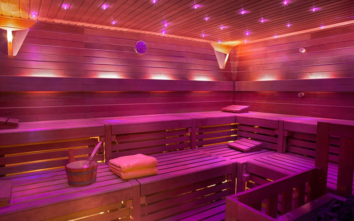 Innenansicht der Sauna im Seaside Grand Hotel Residencia mit Holzbänken und violetter Beleuchtung.