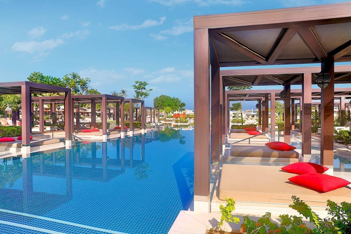 Außenpoolbereich des W Muscat Hotels mit Loungestühlen und roten Kissen.