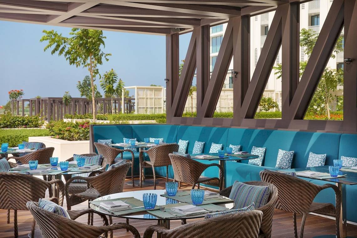 Außenbereich des W Muscat Hotels mit blauen Sofas und Tischen im Freien