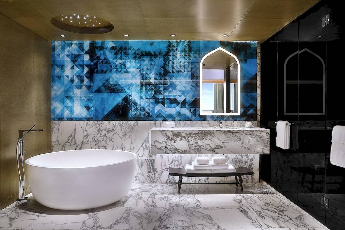 Ein Badezimmer im W Muscat Hotel mit einer blauen abstrakten Wand, einer Badewanne und einem Marmorboden.