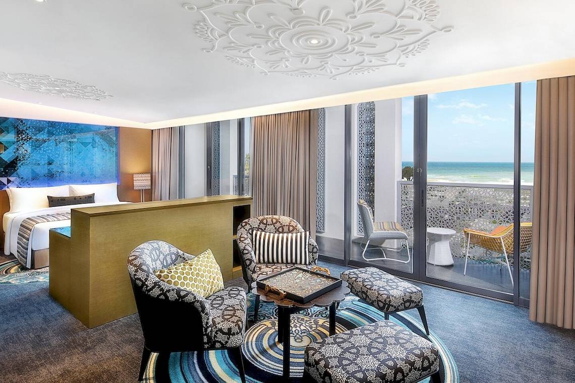 Innenansicht des Hotelzimmers W Muscat mit einem Bett, Wohnzimmerbereich und Blick auf das Meer.