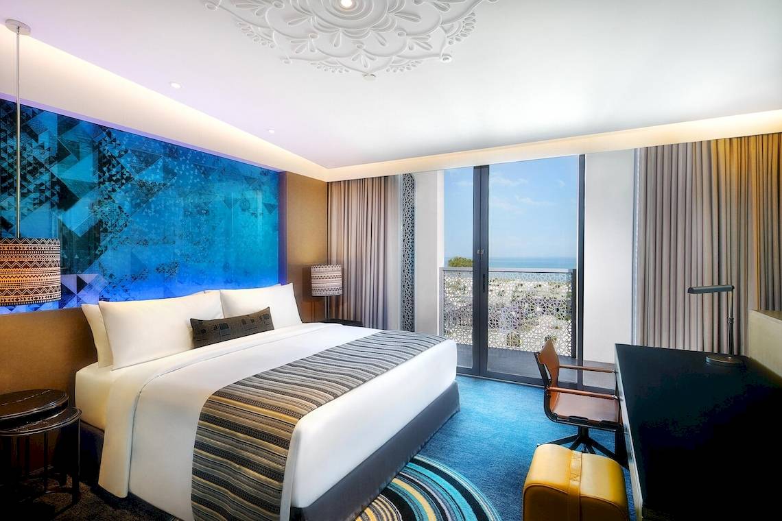 Hotelzimmer im W Muscat mit blauer Wand, Bett, Schreibtisch und Meerblick.