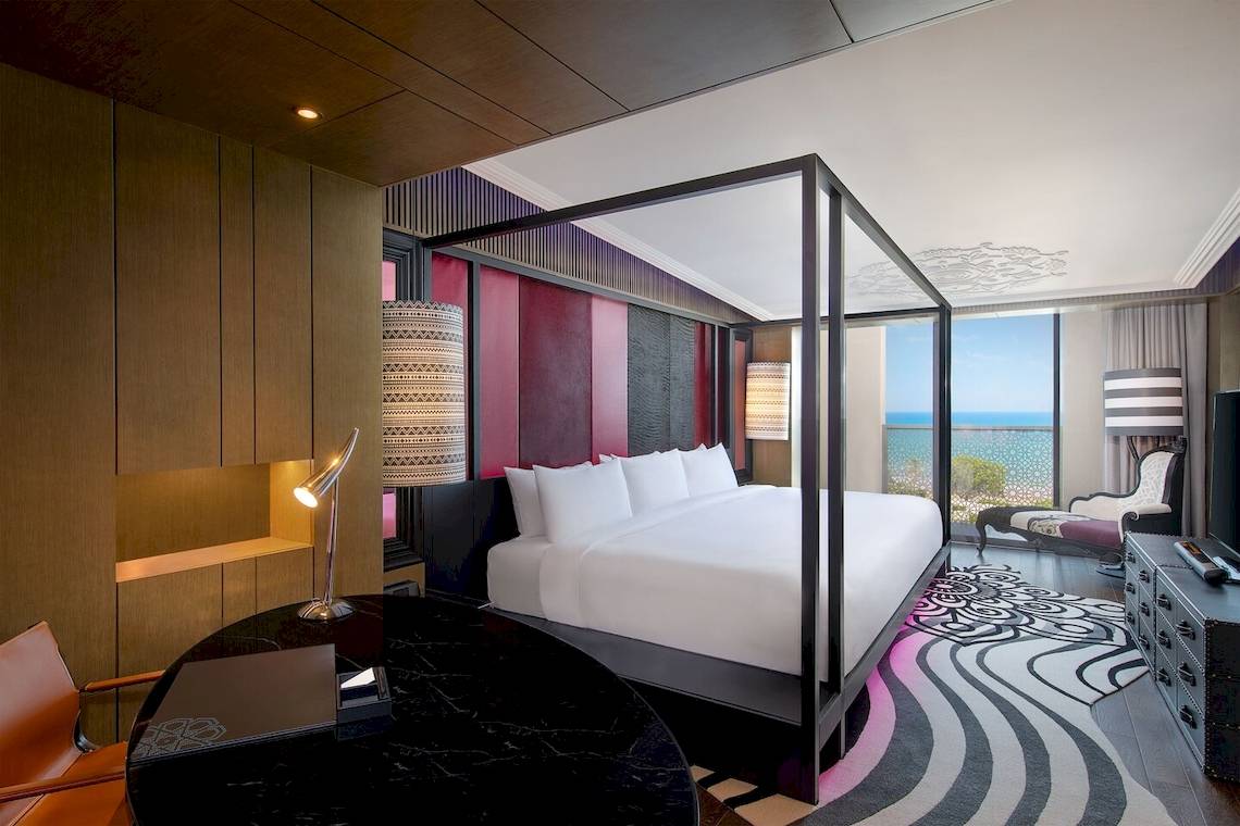 Schlafzimmer im W Muscat Hotel mit Himmelbett, Blick auf das Meer und modernen Möbeln.