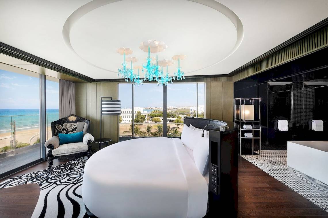 Suite Zimmer im W Muscat mit Blick auf das Meer und eine blaue Kristallkronleuchter.