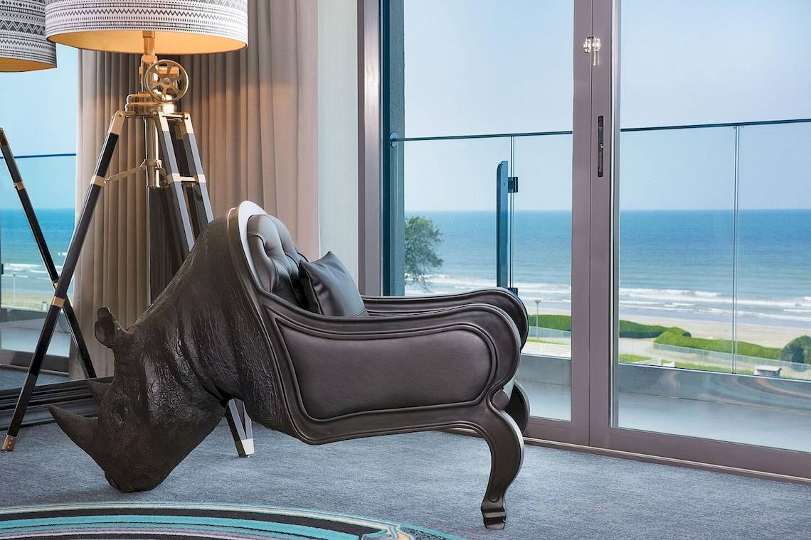 Innenraum des W Muscat mit Meerblick, inklusive Rhino-förmiges Sofa, Lampen und Glastür.