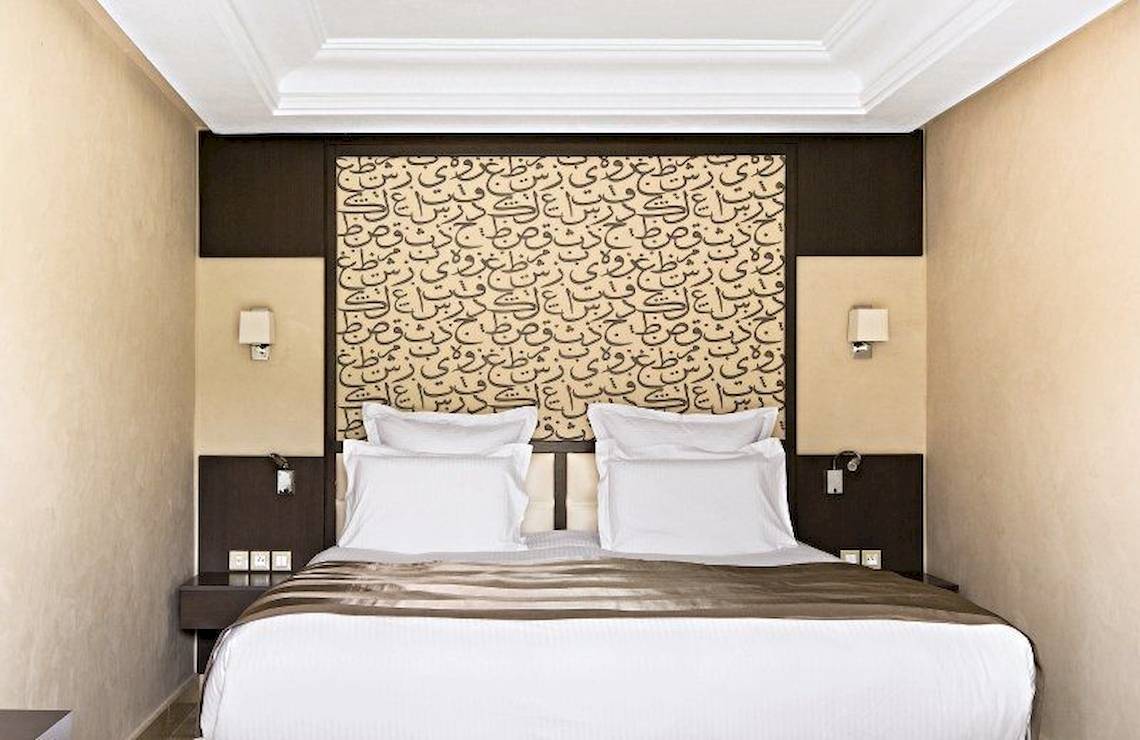 Hotelzimmer im Barcelo Palmeraie mit arabischer Kalligrafie am Kopfende des Bettes.