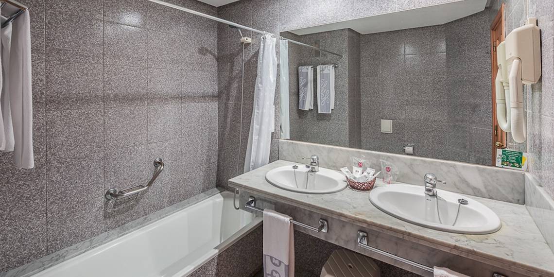 Badezimmer im Puerto Palace Hotel mit Badewanne, zwei Waschbecken, Handtuchhaltern und Spiegel.