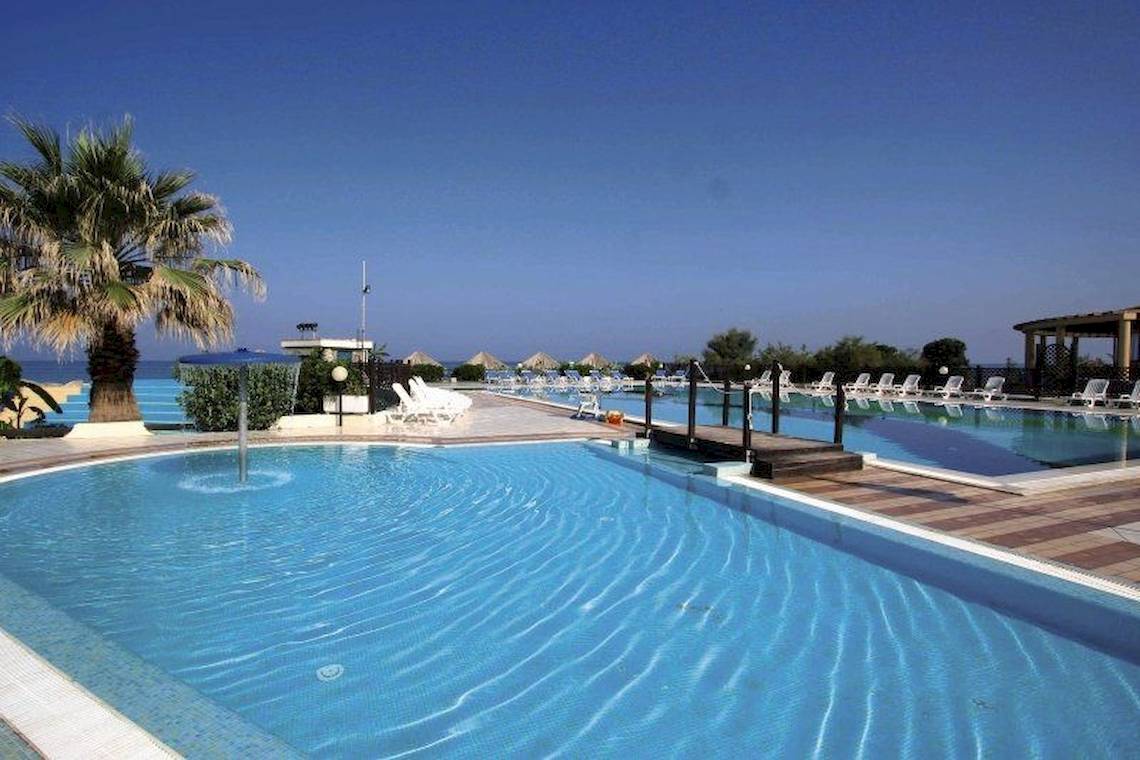 Poolbereich des Villaggio Torre Ruffa Robinson Hotels mit weißen Liegen und Palmen