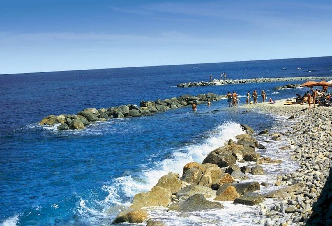 Strand mit Felsen und Meer im Hintergrund, einige Menschen baden und entspannen