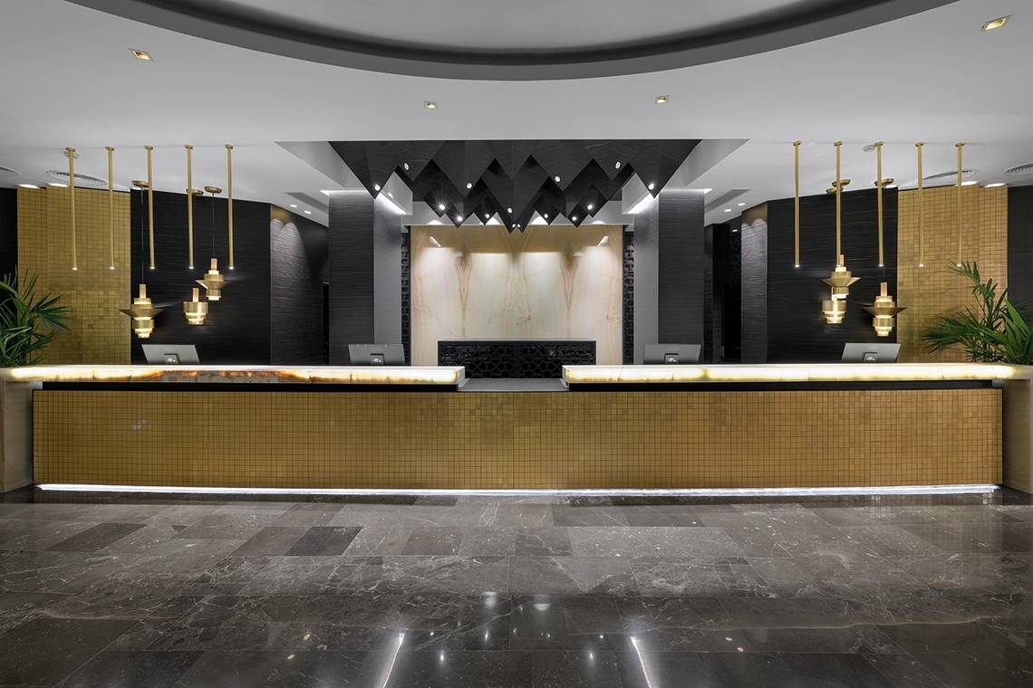 Empfangsbereich des Olympic Palace Resorts mit Marmorboden, goldenen Pendelleuchten und Rezeptionstresen.