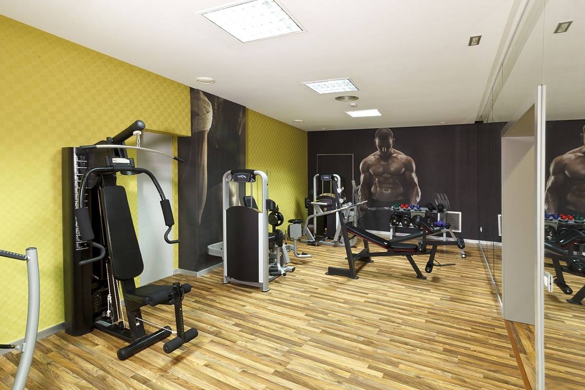 Fitnessraum im Olympic Palace Resort mit modernen Geräten und gelben Wänden.