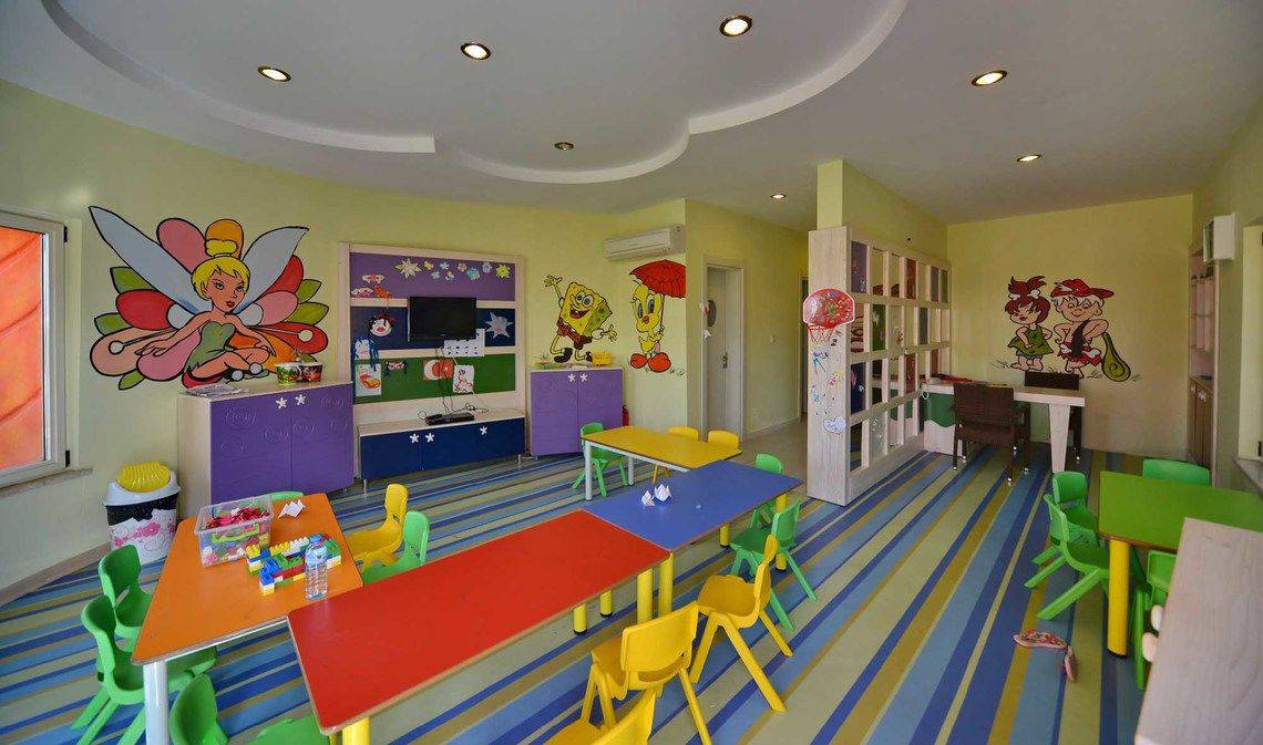 Kinderzimmer mit bunten Tischen und Stühlen, illustrierte Wände und Klimaanlage.