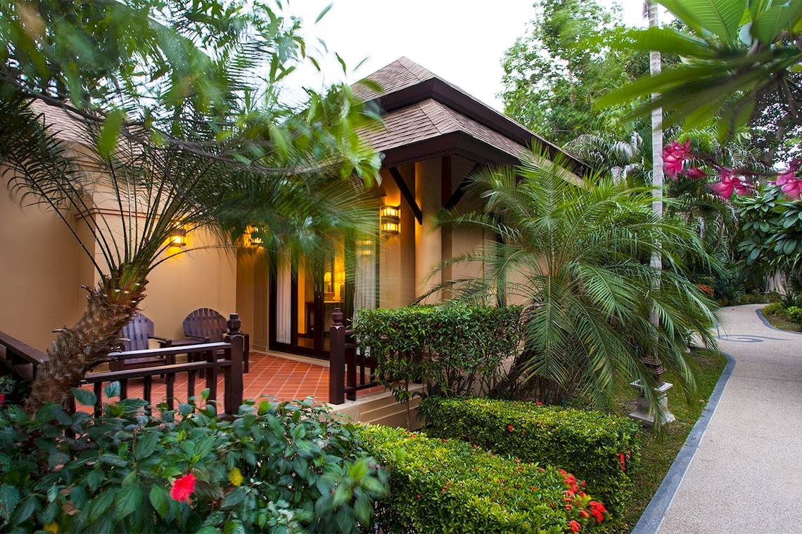 Außenansicht der Fair House Beach Resort Villa mit Terrasse, Garten und Gehweg.