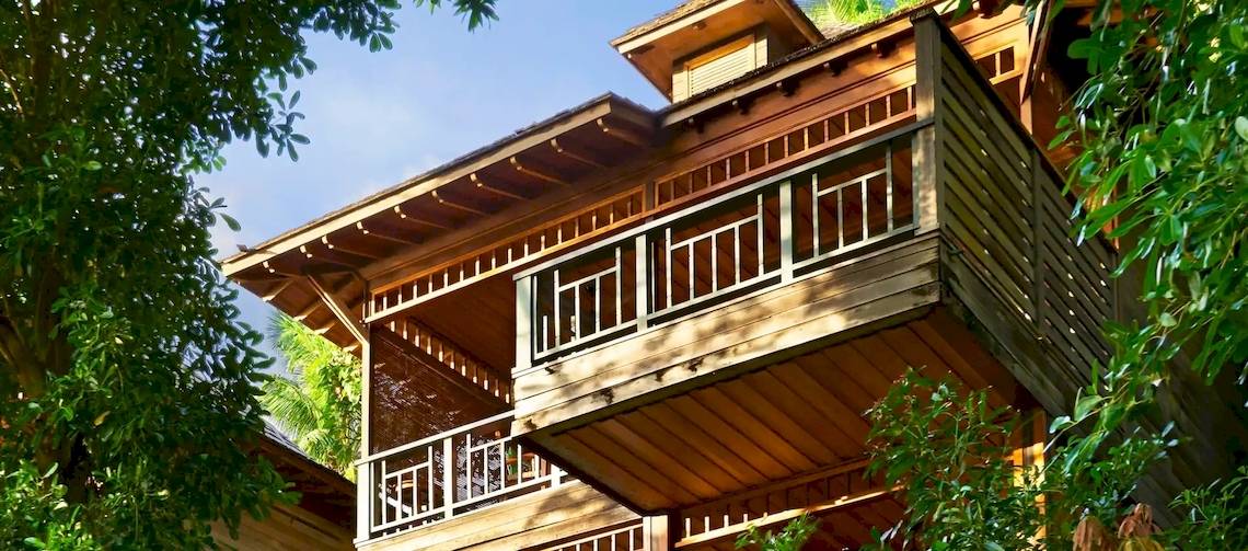 Ein zweistöckiges Holzhaus mit Balkon, umgeben von Bäumen, im Hilton Seychelles Northolme Resort & Spa.