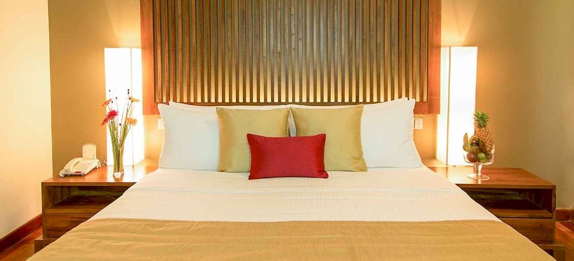 Hotelzimmer im Occidental Eden Beruwala mit Bett, Kissen, Nachttischen und Dekoration.