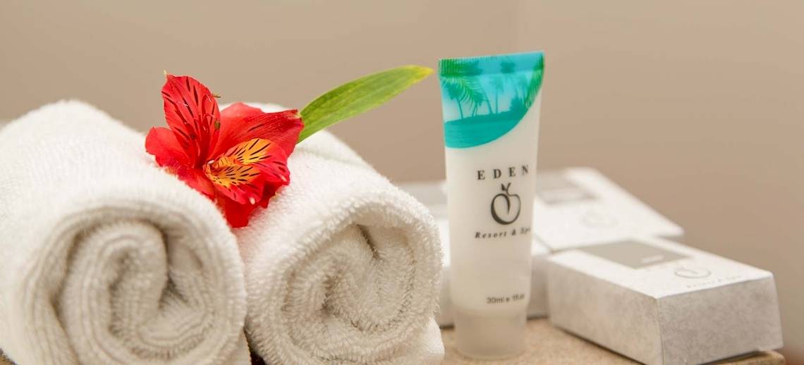 Zwei weiße Handtücher mit einer roten Blume und einem kosmetischen Produkt auf einem Tisch im Occidental Eden Beruwala Hotel.