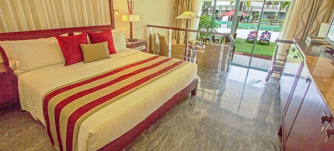 Hotelzimmer im Occidental Eden Beruwala mit großem Bett, roten Kissen, und Glasbalkon.