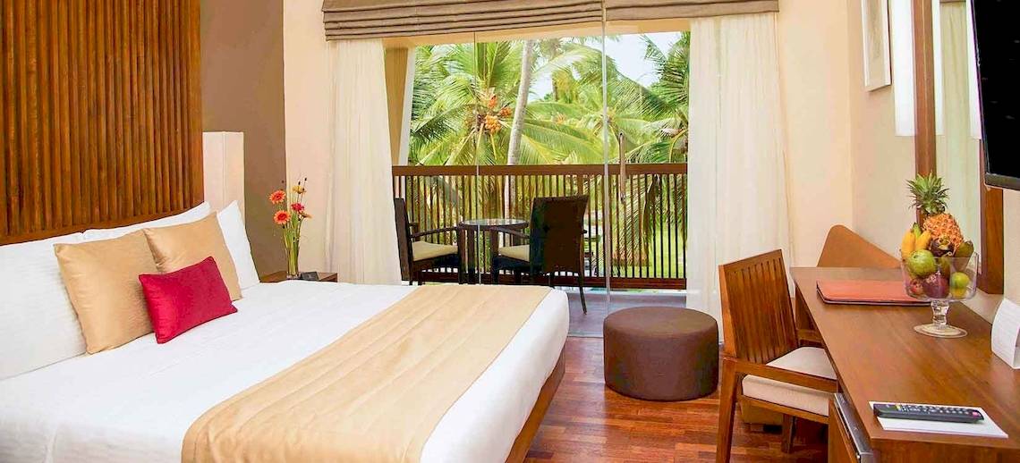 Hotelzimmer des Occidental Eden Beruwala mit einem Bett, Balkon und Aussicht auf Palmen.