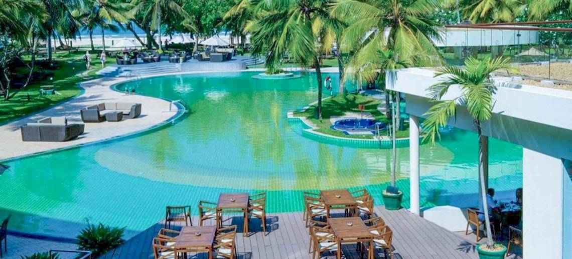Außenpool und Terrasse des Occidental Eden Beruwala Hotels mit Tischen, Stühlen und Loungemöbeln.
