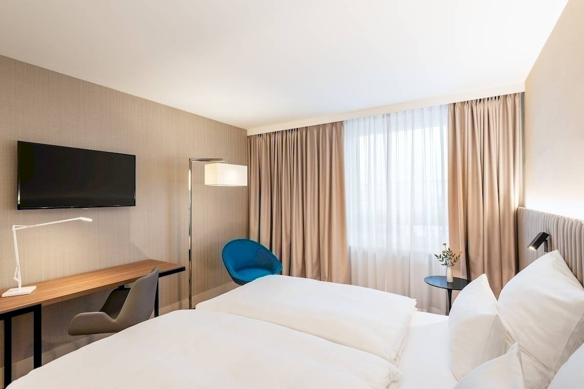 Innenansicht eines Doppelzimmers im NH Hamburg Altona mit zwei Betten, Schreibtisch und Fernseher.