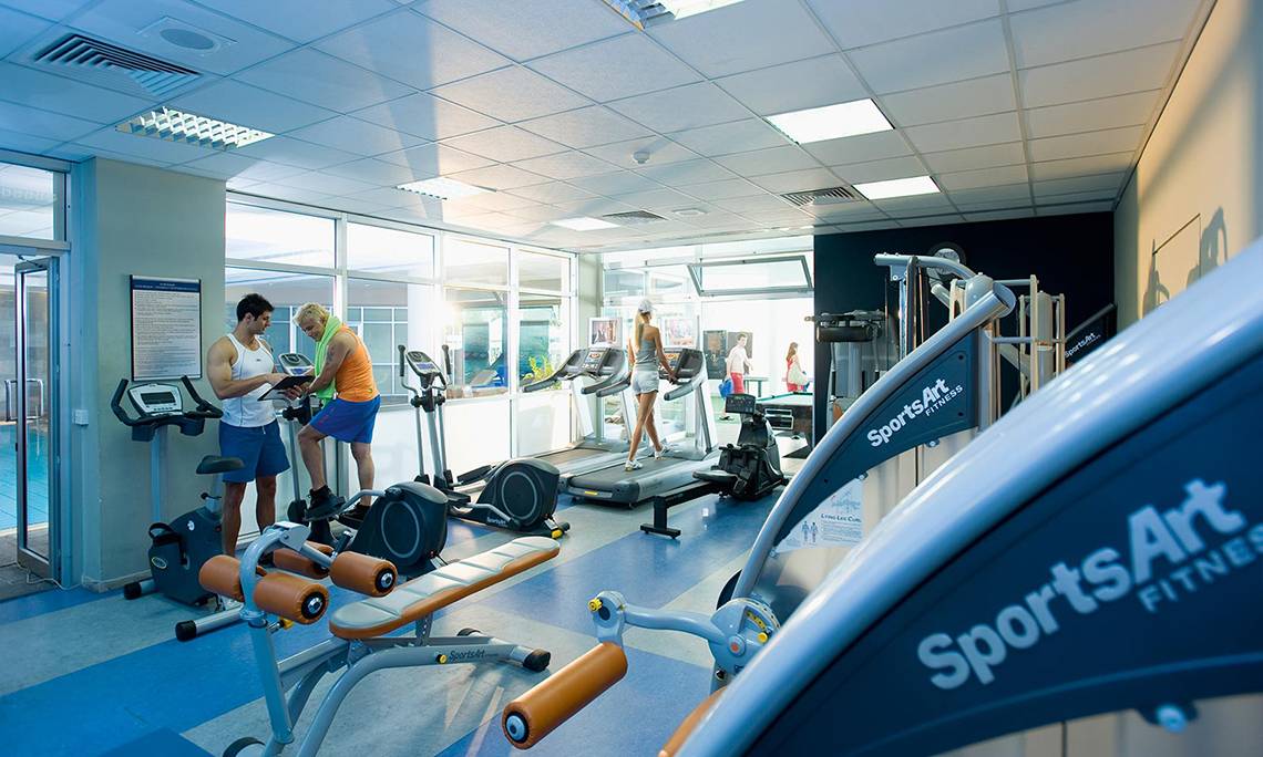 Fitnessstudio im Mediterranean Beach Hotel Zypern mit mehreren Trainingsgeräten und Personen.