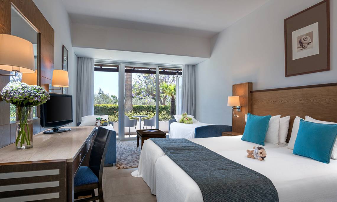 Doppelzimmer im Mediterranean Beach Hotel in Zypern mit zwei Betten, Fernseher, Schreibtisch und Balkonzugang.