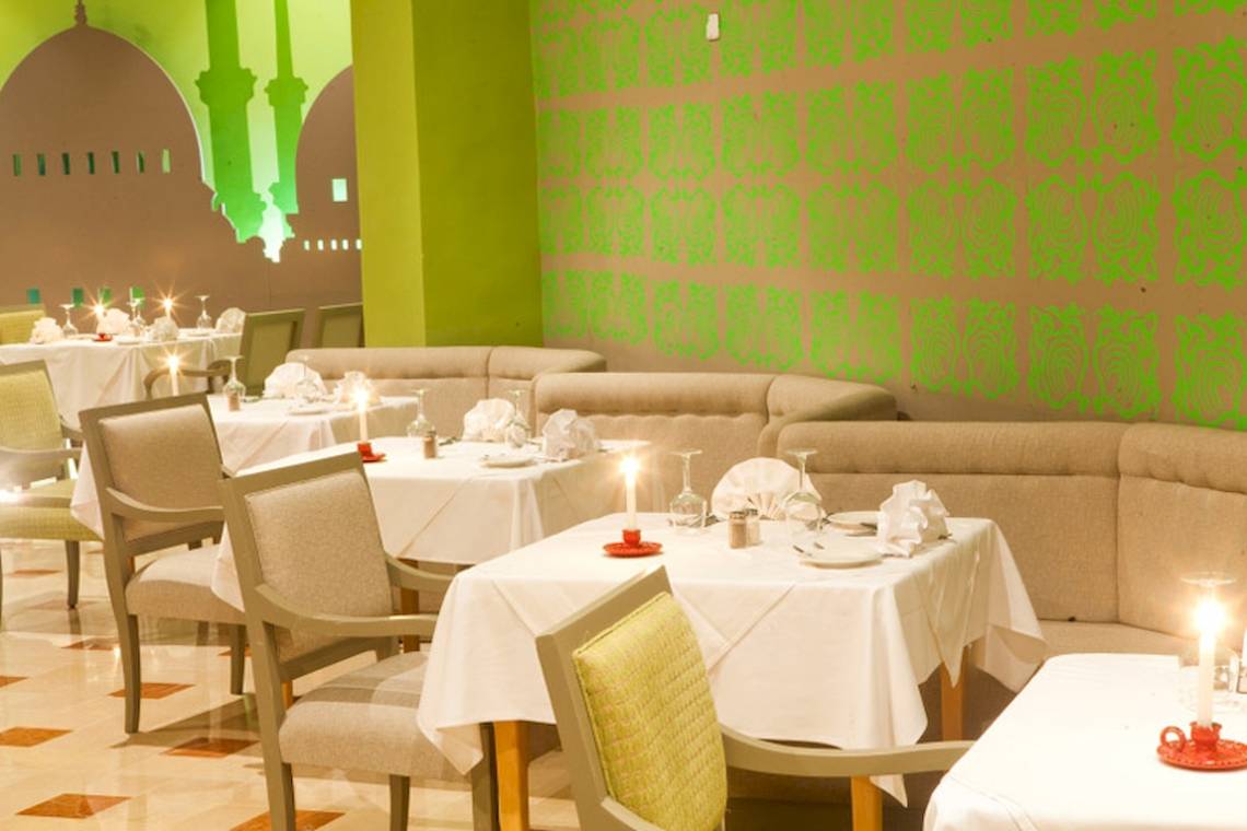 Restaurant im El Mouradi Hammamet Hotel mit grünen Wänden und gedeckten Tischen.