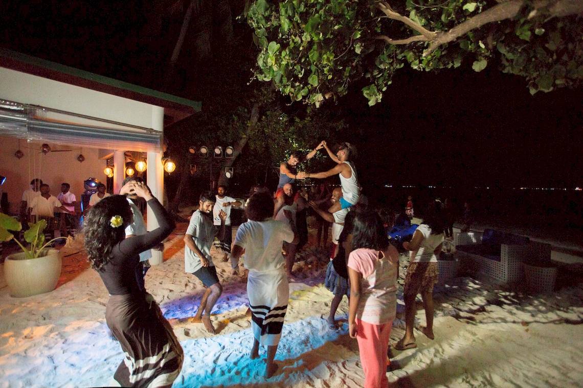 Menschen tanzen in der Nacht am Strand des Malahini Kuda Bandos Resorts.