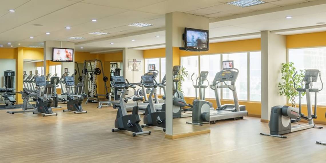 Fitnessstudio im Tower Plaza Hotel Dubai mit vielen Geräten und Fernsehern an der Wand.
