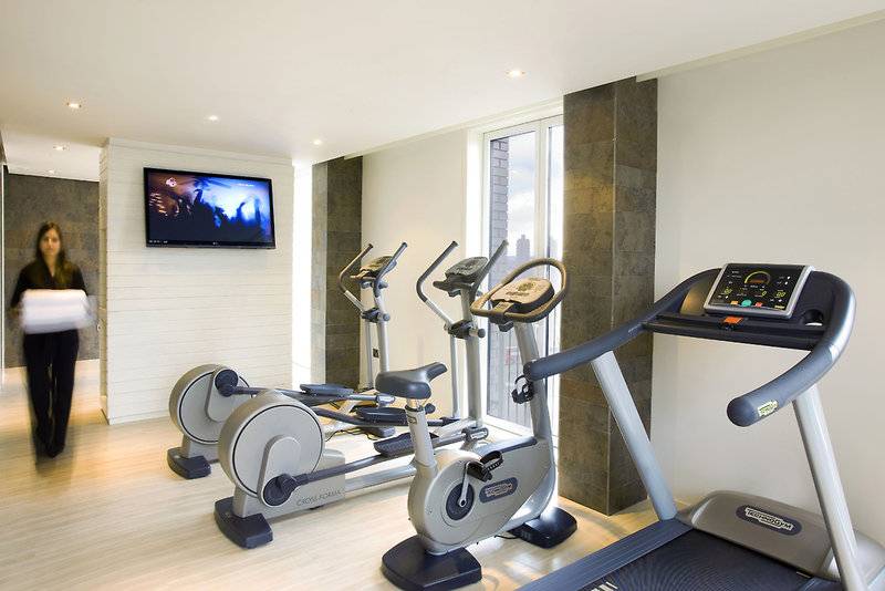 Fitnessraum im H10 London Waterloo mit Geräten und Fernseher an der Wand.