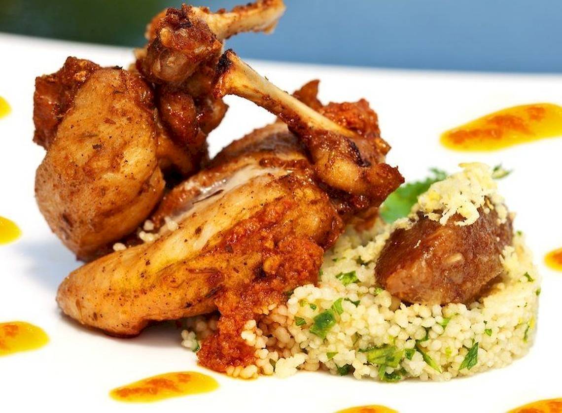 Gebratenes Huhn mit Couscous und Soßen auf einem weißen Teller serviert.