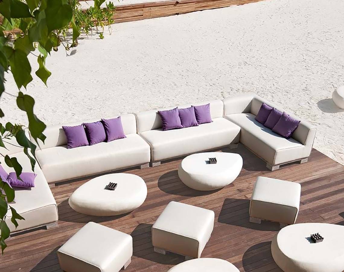 Loungebereich am Strand des Constance Moofushi Maldives Hotels mit weißen Möbeln und Kissen.