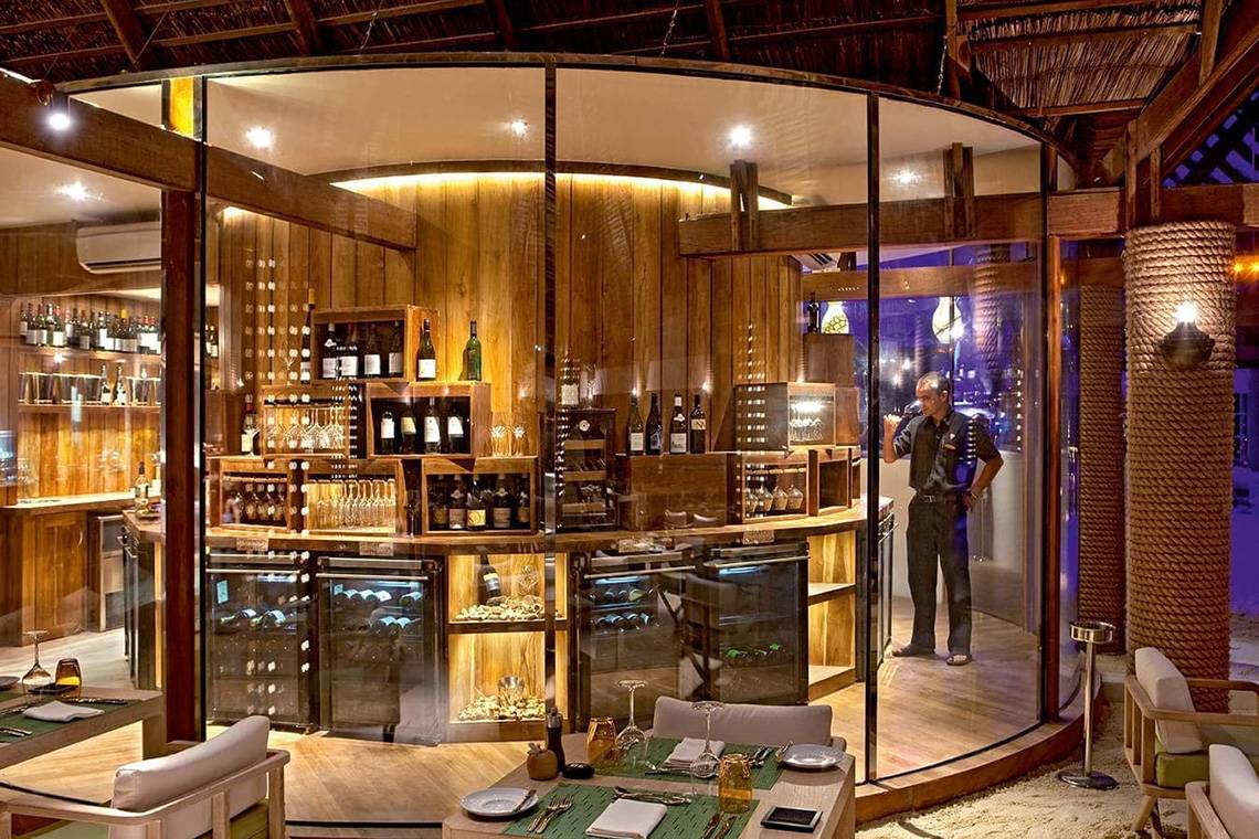 Ein Barbereich im Constance Moofushi Maldives Hotel mit einem Mann, der hinter einer Glasscheibe steht.