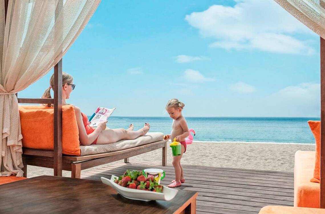 Eine Frau liest auf einer Terrasse im Aska Lara Resort & Spa, während ein Kind daneben spielt.