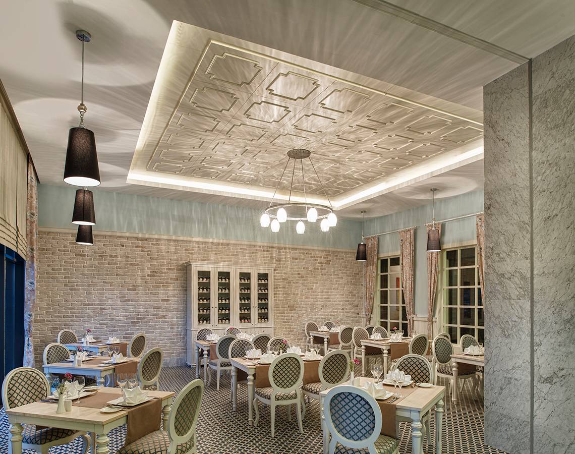 Innenansicht des Restaurants im Aska Lara Resort & Spa mit Tisch, Stühlen und dekorativen Deckenleuchten.