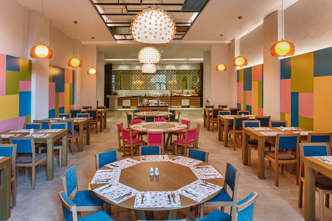 Innenbereich eines Restaurants im Aska Lara Resort & Spa mit bunten Wänden und runden Tischen.
