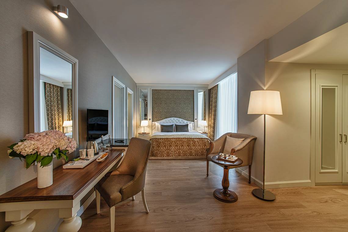 Innenansicht eines Hotelzimmers im Aska Lara Resort & Spa mit Schreibtisch, Stühle und Bett.