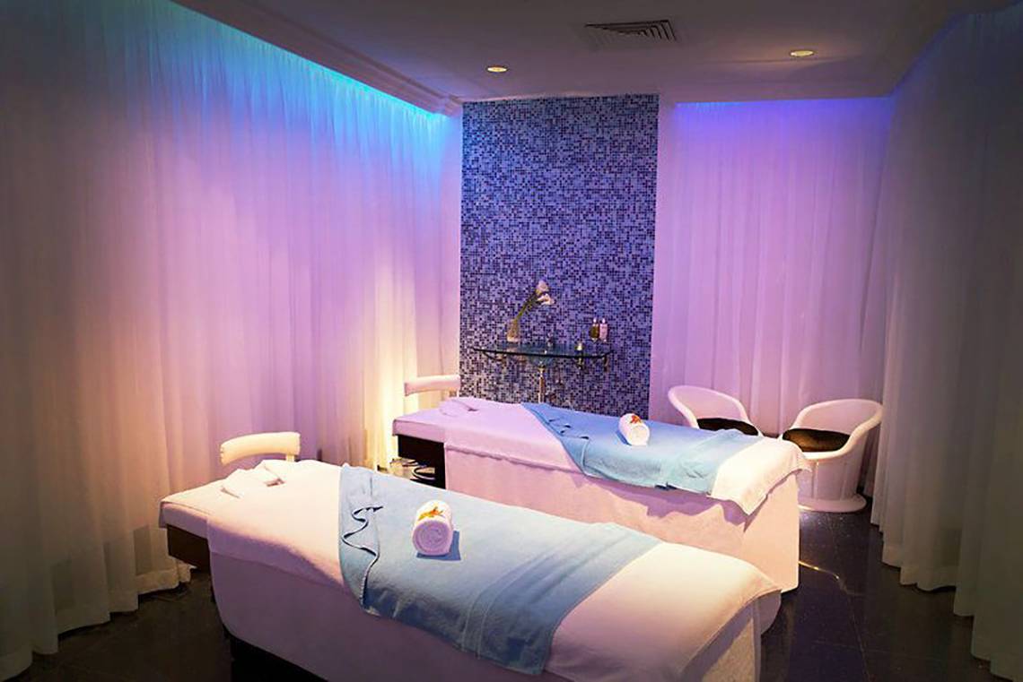 Massageraum im JA Ocean View Hotel mit zwei Massagetischen, blauen Kissen und weißen Stühlen.